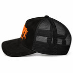 A black trucker-style cap with a black mesh back and a curved black brim, featuring a prominent orange graphic logo embroidered on the front suede-style panel.