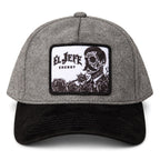 A heather gray and black baseball cap featuring a rectangular front patch with the text 'EL JEFE ENERGY' and a black-and-white illustration of a skull-faced figure with roses.