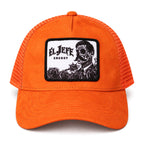 An orange trucker hat with a black and white embroidered patch on the front that reads 'El Jefe Energy' and features a skeleton face illustration. The hat has orange mesh side panels and is shown against a plain white background.
