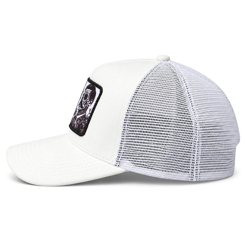 A white suede trucker-style cap with a white mesh back and a black rectangular patch on the side featuring a graphic of a skull.