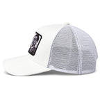 A white suede trucker-style cap with a white mesh back and a black rectangular patch on the side featuring a graphic of a skull.